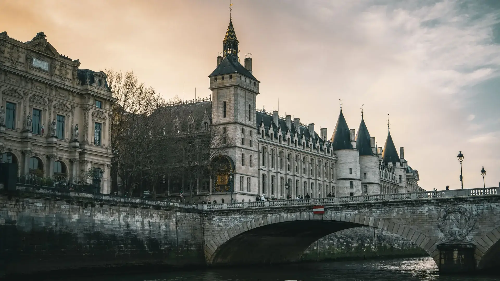 The Conciergerie's clock tower and conical towers above the Seine at dusk, seen from the river beneath the Pont au Change